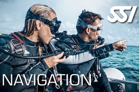 Two scuba divers in wetsuits on a boat, one points towards the sea. SSI logo and 'Navigation' text visible.
