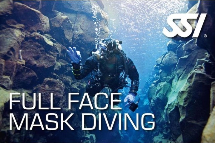 Scuba diver in full face mask swimming between rocks underwater, SSI logo visible.