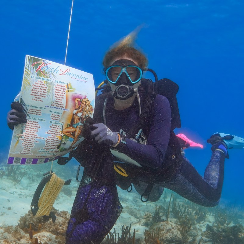 Scuba diver underwater holding a menu with coral in the background.